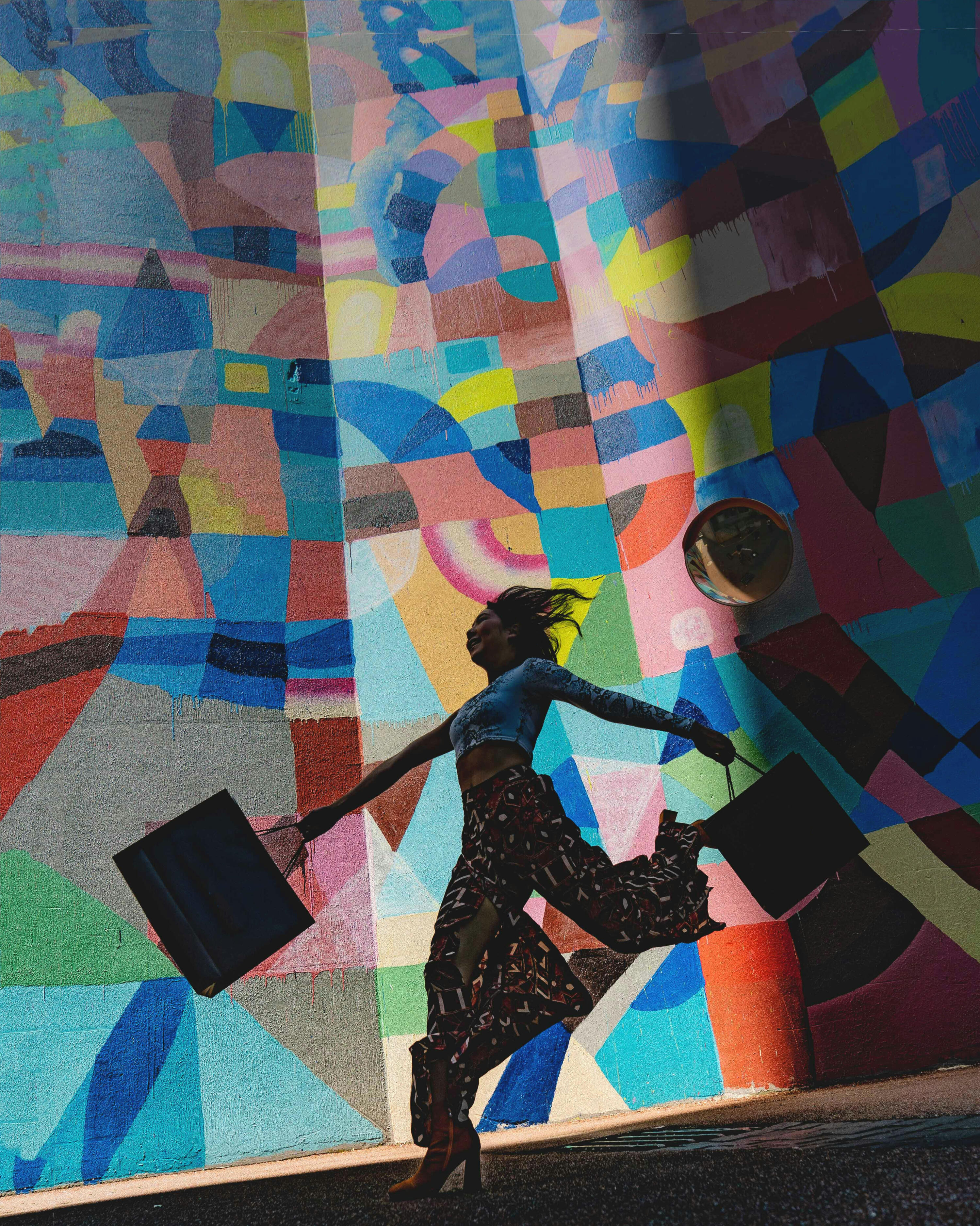 A woman joyfully skipping down a road in front of a colorful mural. Her expression and energy matches the vibrancy of the mural in the background.